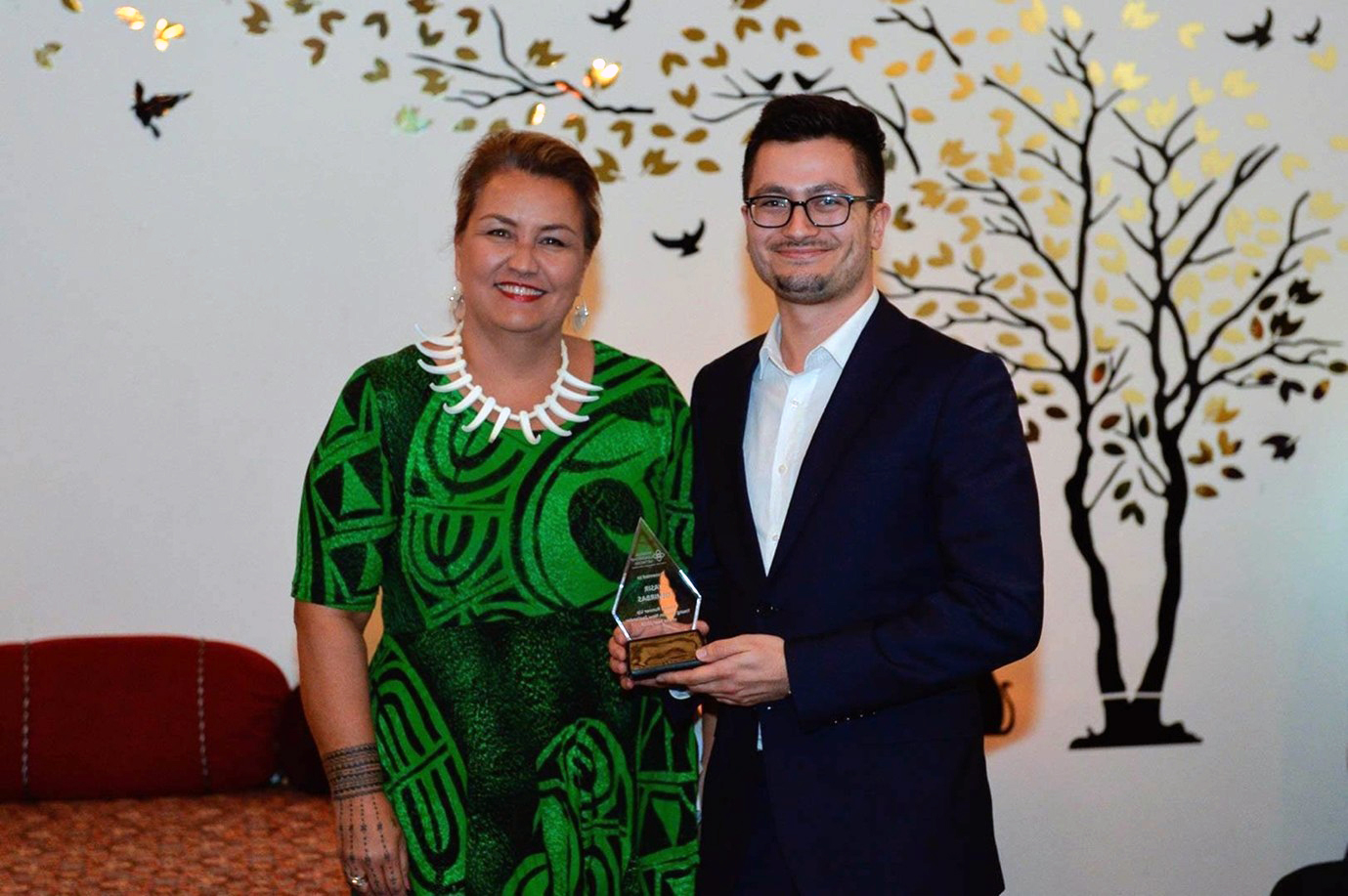 Assir reciving stadning beside a woman holding an award