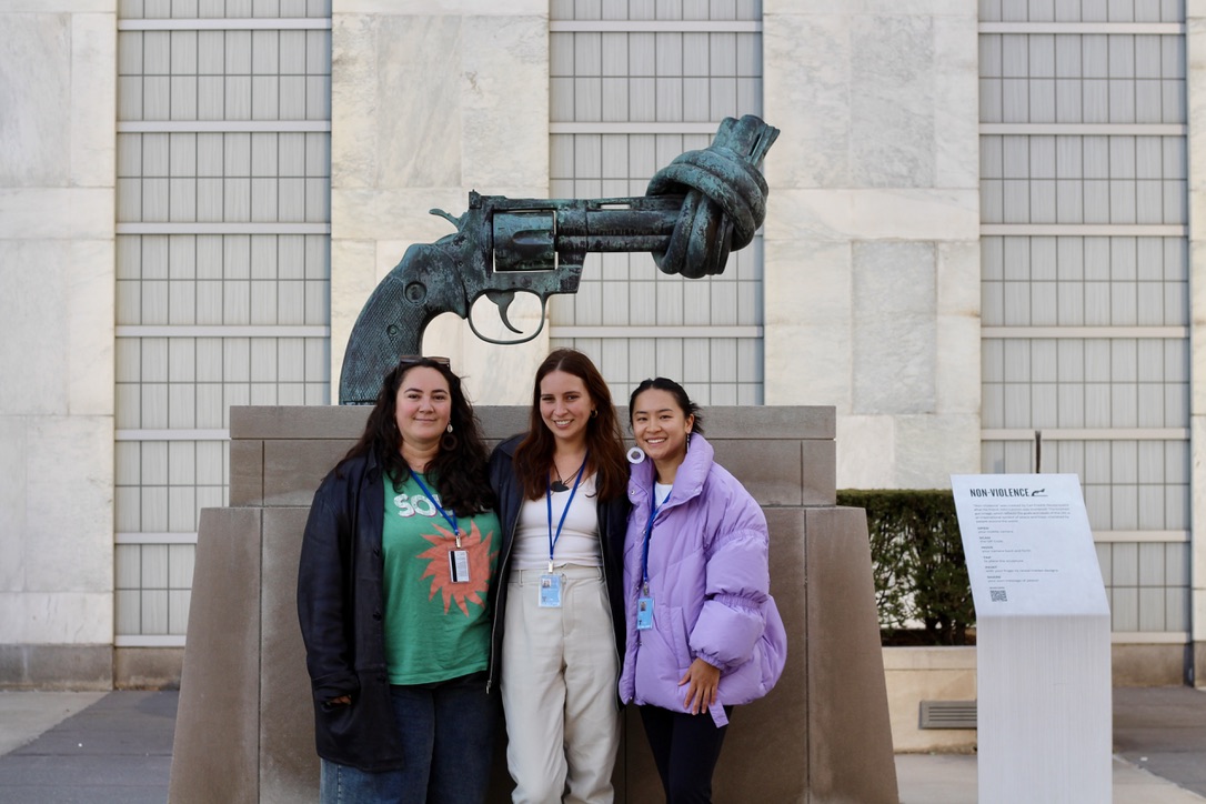 Terressa and two other peole pose in front of a sculpture of a pistol with a knot tied in the barrel