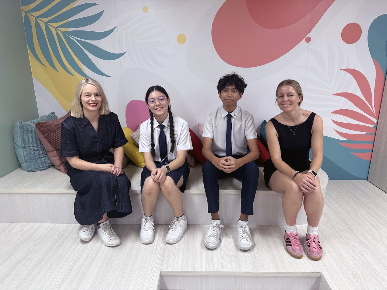 A teacher and three students sitting on a bench in front of a colourful mural
