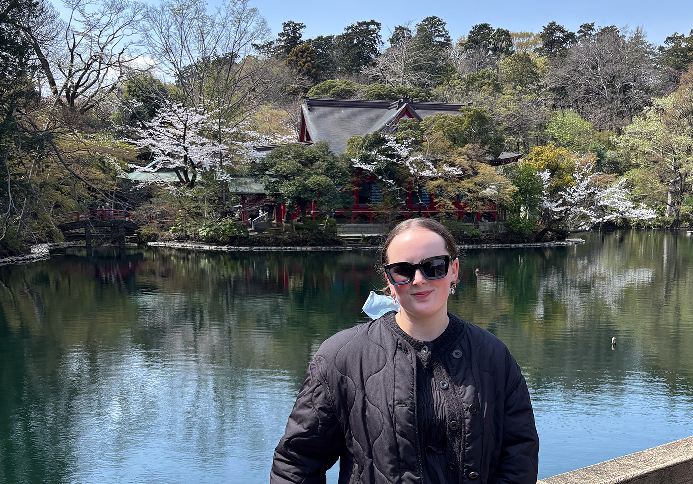 Grace standing in front of a lake with cherry blossoms flowering behind her