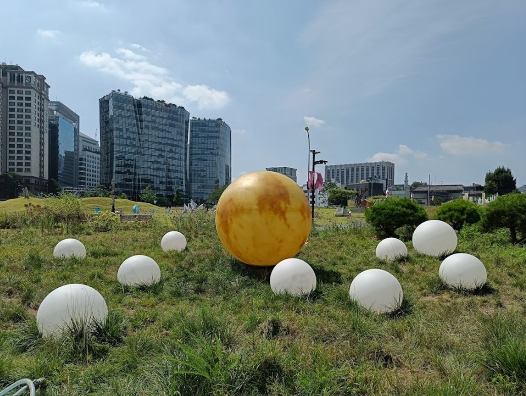 An outdoors artwork installation of a large yellow ball surrounded by smaller white balls on city park