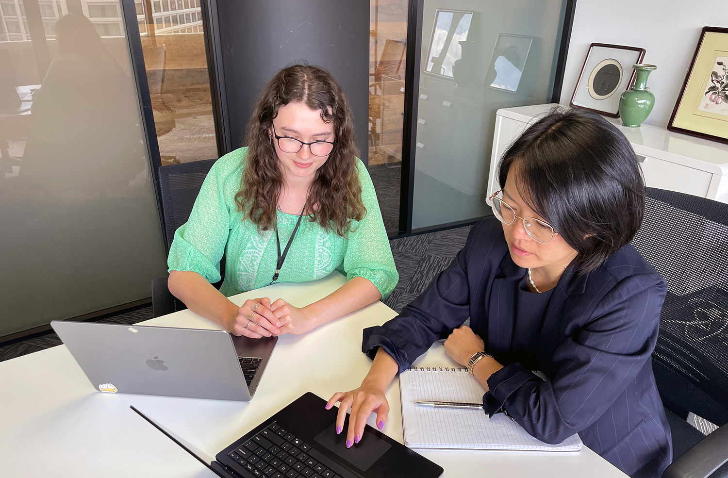 Emilia and a woman sitting at a desk looking at their laptops