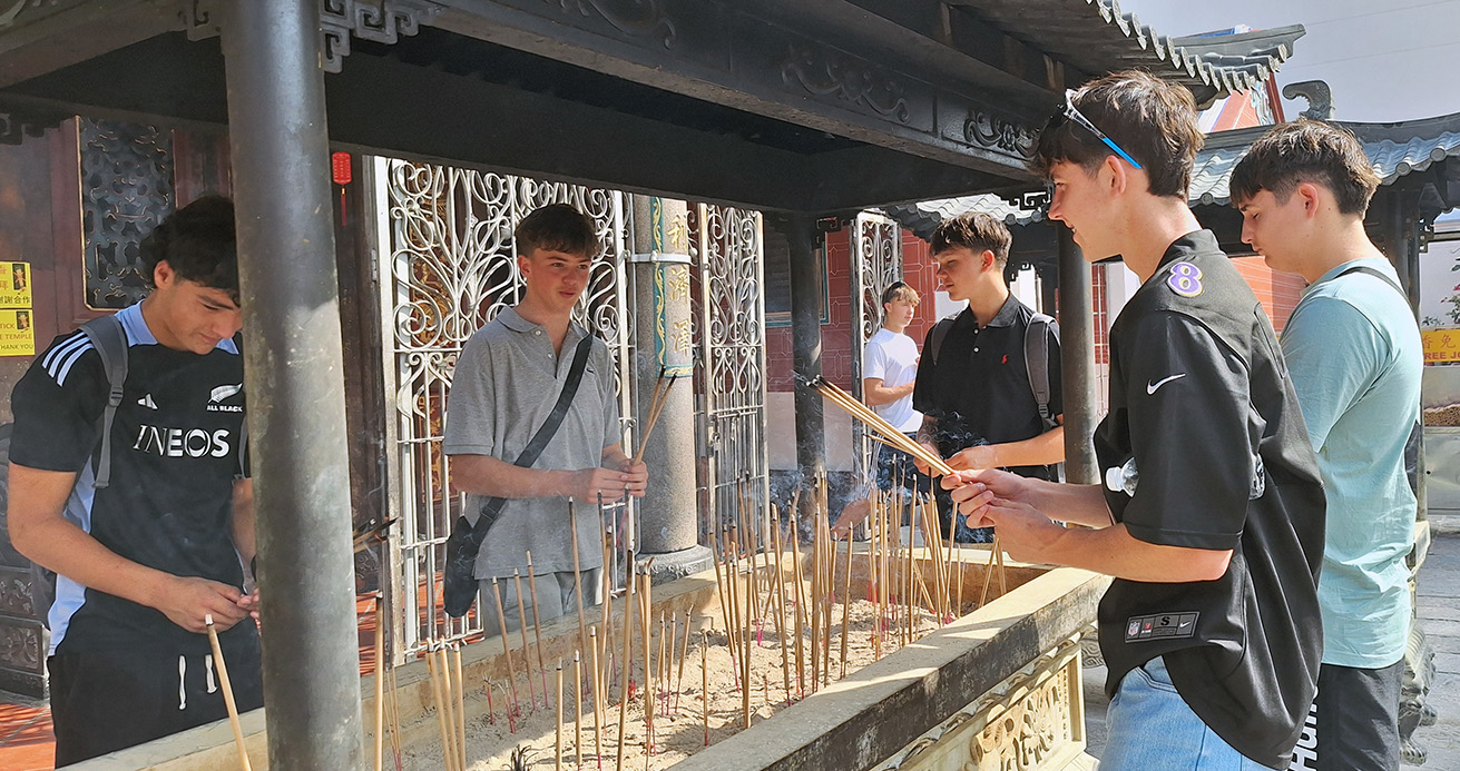 Team members putting incense sticks into sand at a shrine