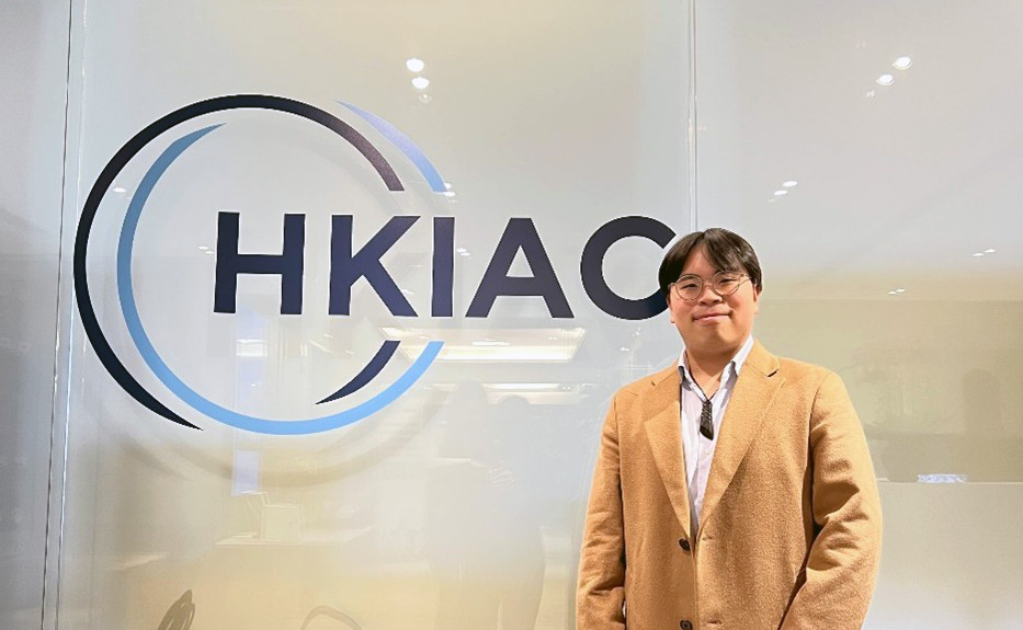 Ryan standing in front of an HKIAC sign on glass panels