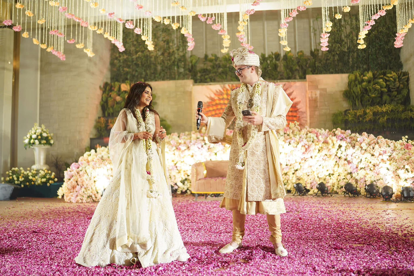 Anisha and Brent on stage dressed in their wedding attire with Brent holding a microphone
