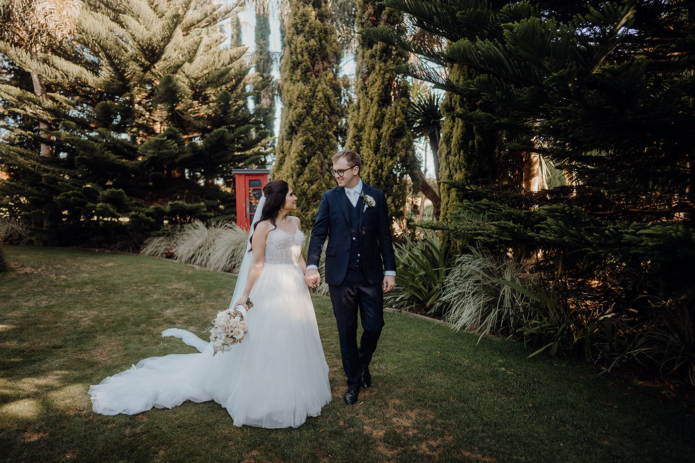 A photo of Anisha and Brent in their New Zealand wedding outfits walking through a garden