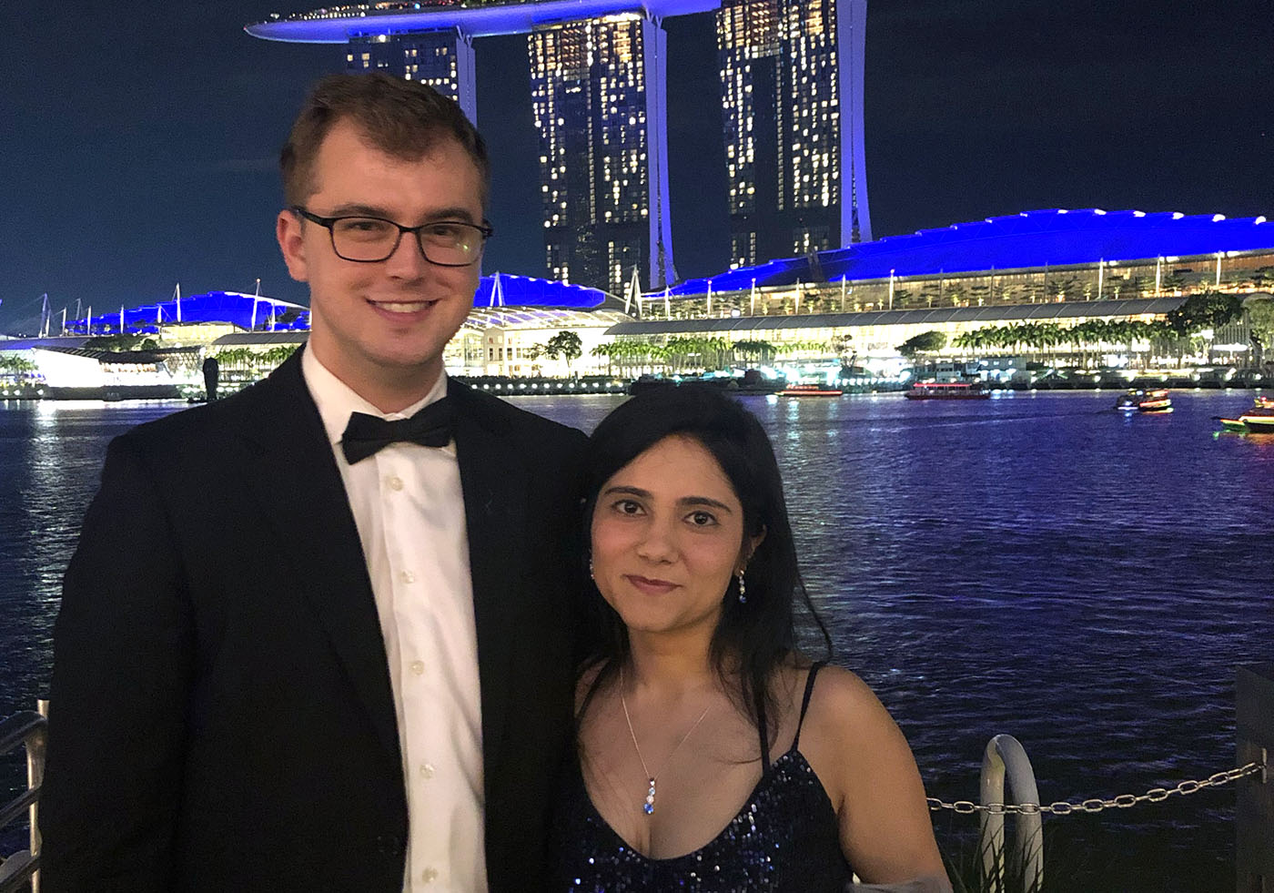 Brent and Anisha standing together in front of Singapore Harbour with a large building in the background