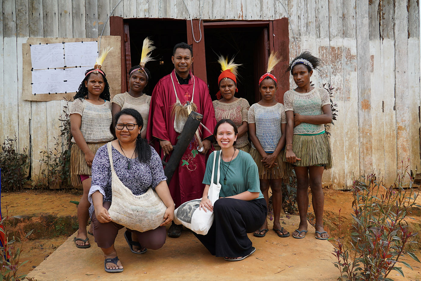 Katja with a group seven people (some in traditional Papuan dress) posing for a group photo outside a shed