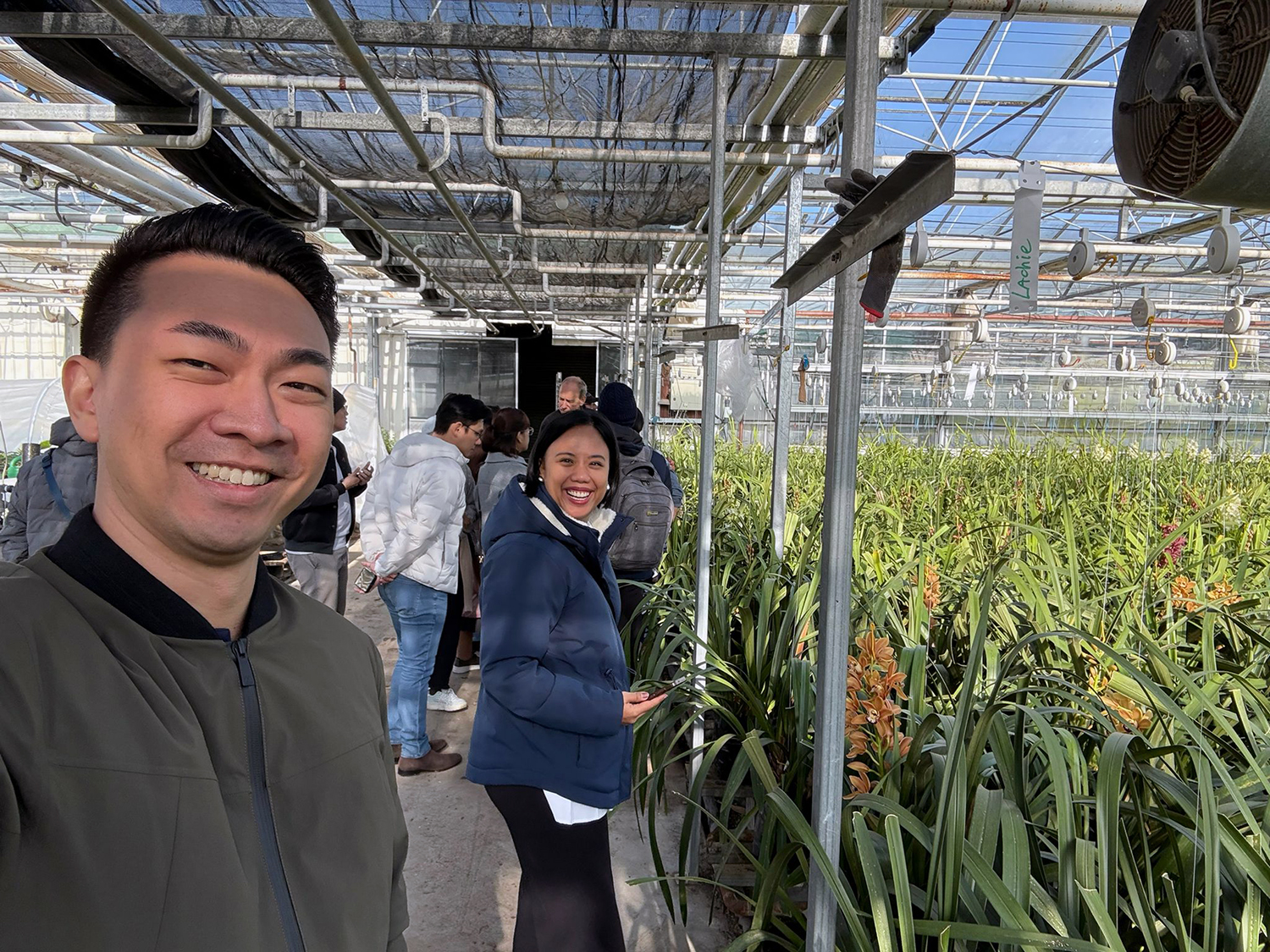 Two of the entrepreneurs smiling at the camera in a large greenhouse full of flax-like plants