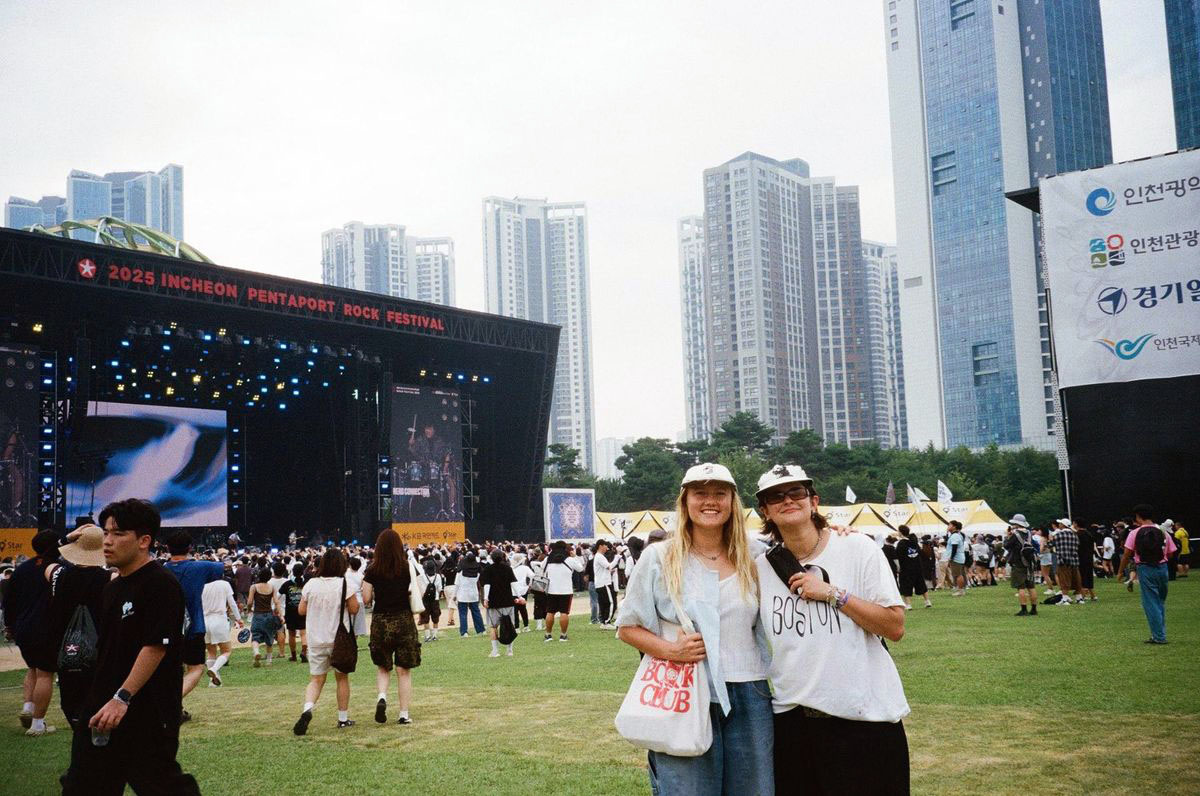 Two of the band posing for a photo at an outdoor music festivak, with the stage behind them