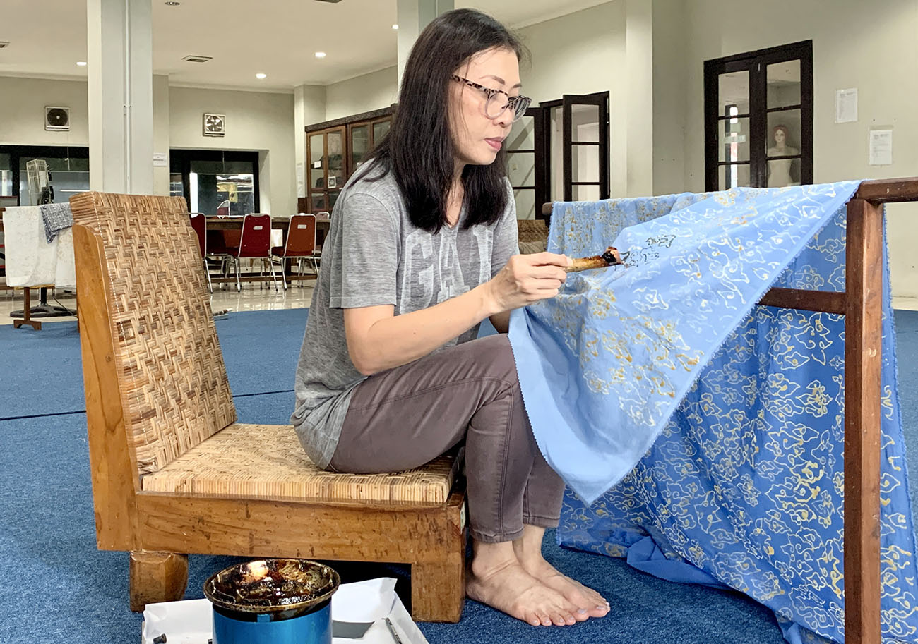 Rosana sitting on a chair working on a piece of blue material