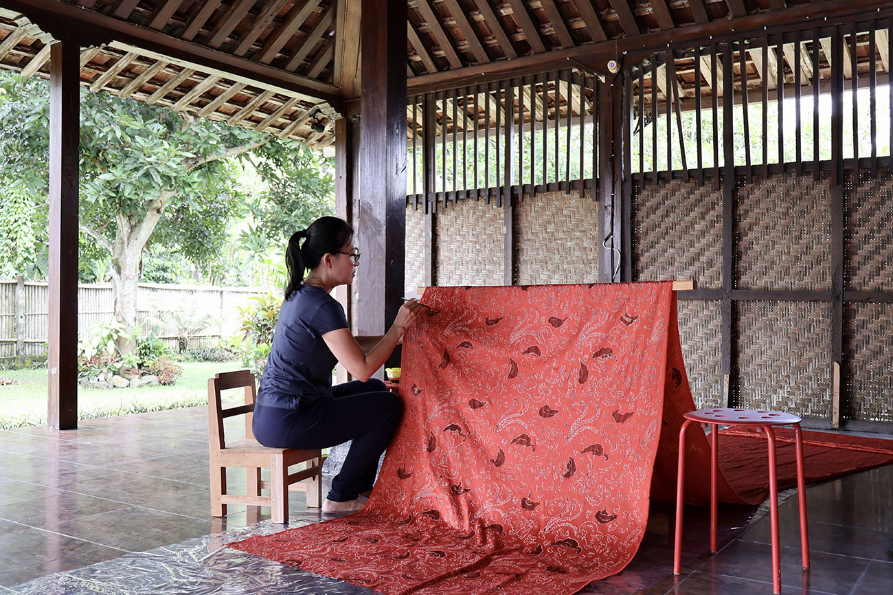 Rosana sitting on a chair working on a piece of red batak material
