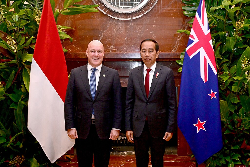 New Zealand Prime Minister Christopher Luxon met with (now former) Indonesian President Joko Widodo standing between their nations flags