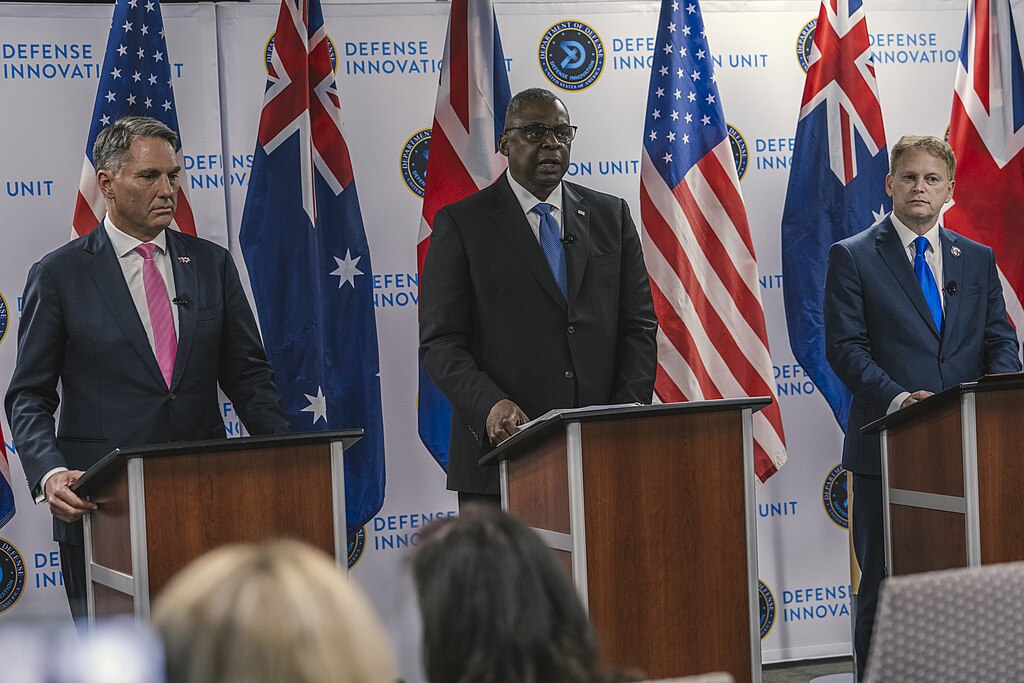 Defence ministers from AUKUS countries - The United States, the UK and Australia - standing on stage in front of their national flags