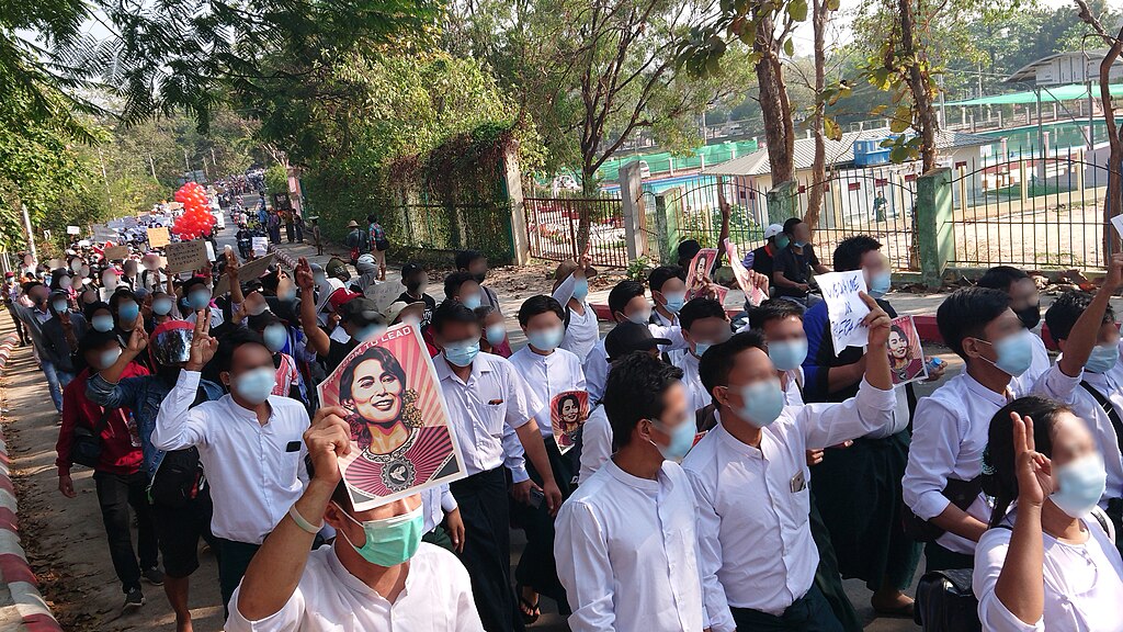 Teachers wearing masks, some carrying photos of  Aung San Suu Kyi, marching down a street