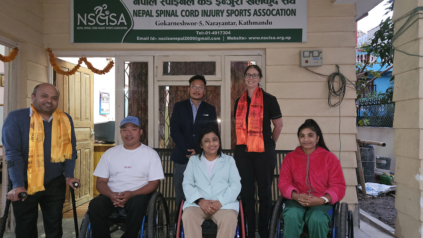 Dr Harris with members of the Nepal Spinal IUnjury Assiciation in front of the associations sign