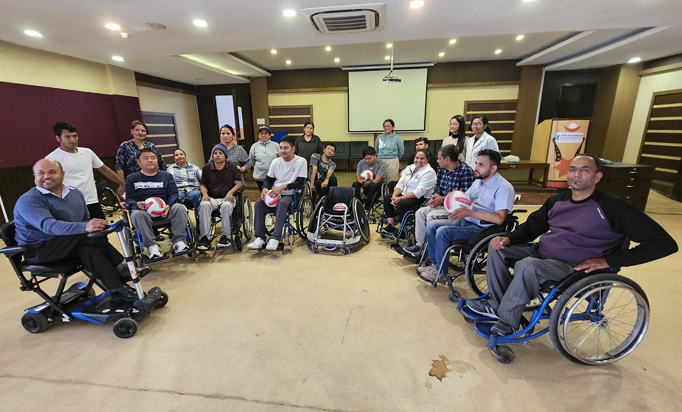 A group of people in wheelchairs, some holding volley-ball-style balls posinf for a photo