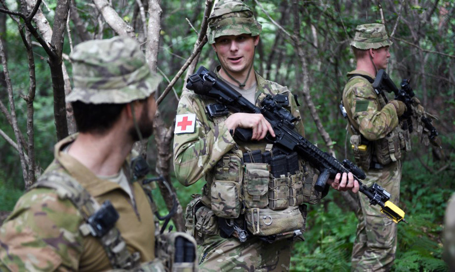 Three soldiers standing in scrub while holding their rifles