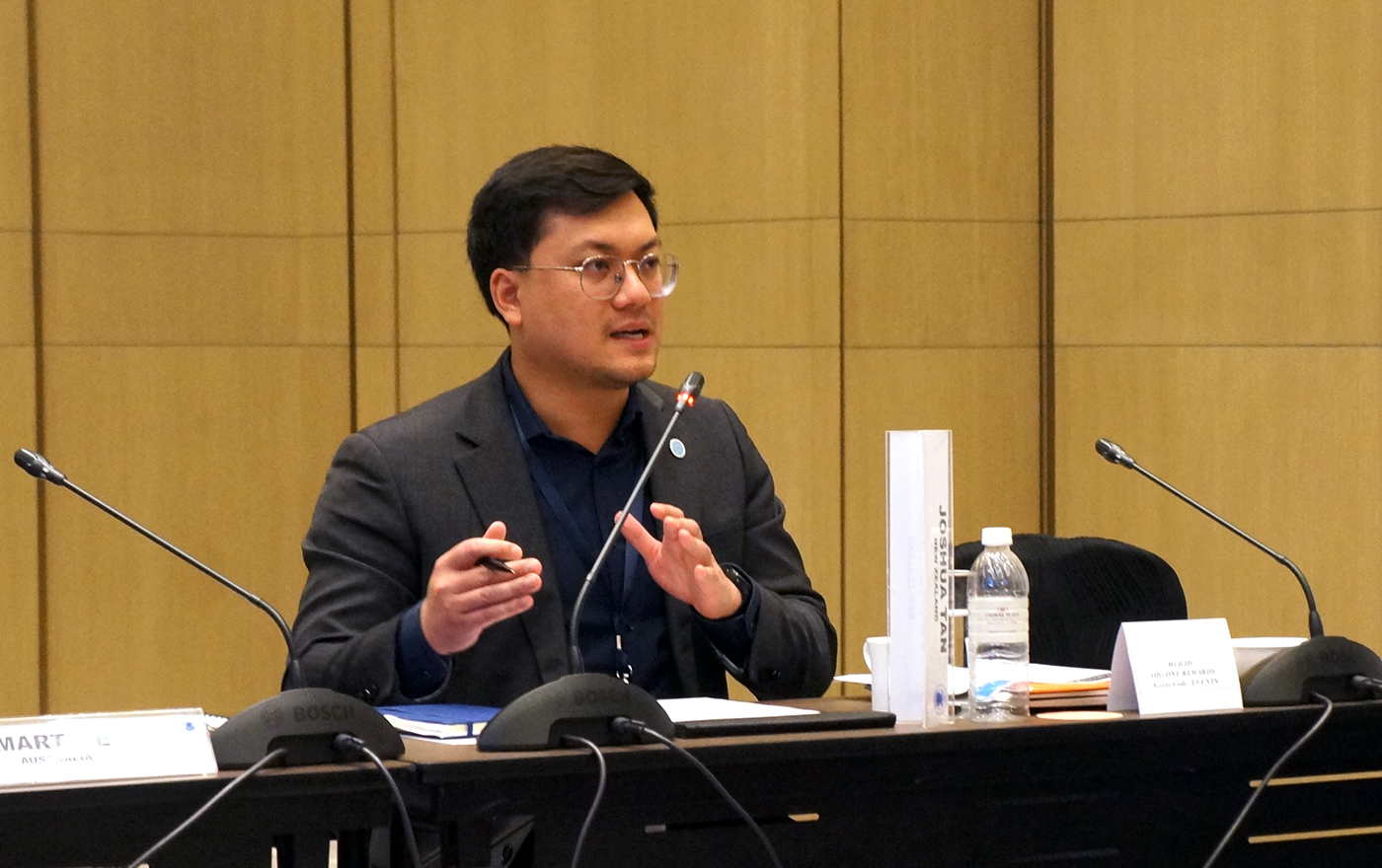 Josh Tan sitting at a conference table speaking into a microphone