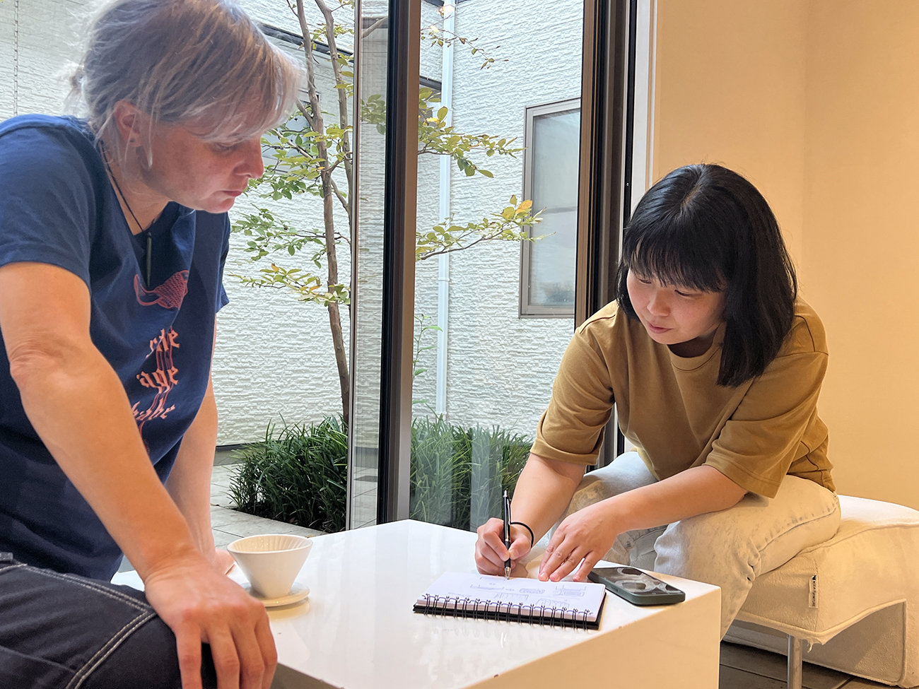 Ngaroma watches as Artist Misato Sano draws diagrams to explain joinery techniques