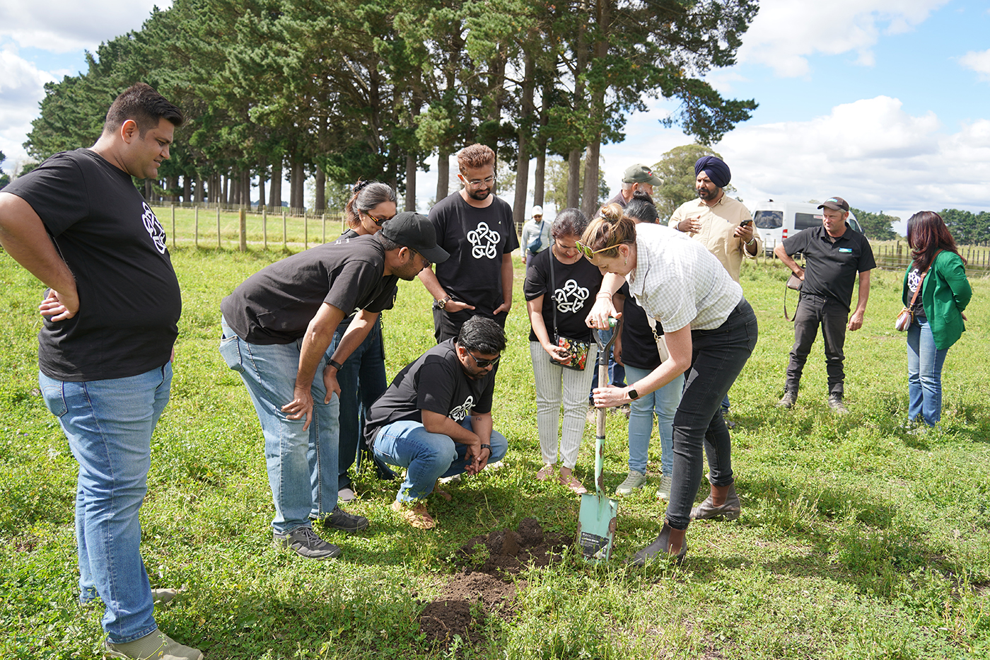 The Indian entrepreneurs who visited New Zealand with the Foundation standing in a paddock as a woman digs a hole
