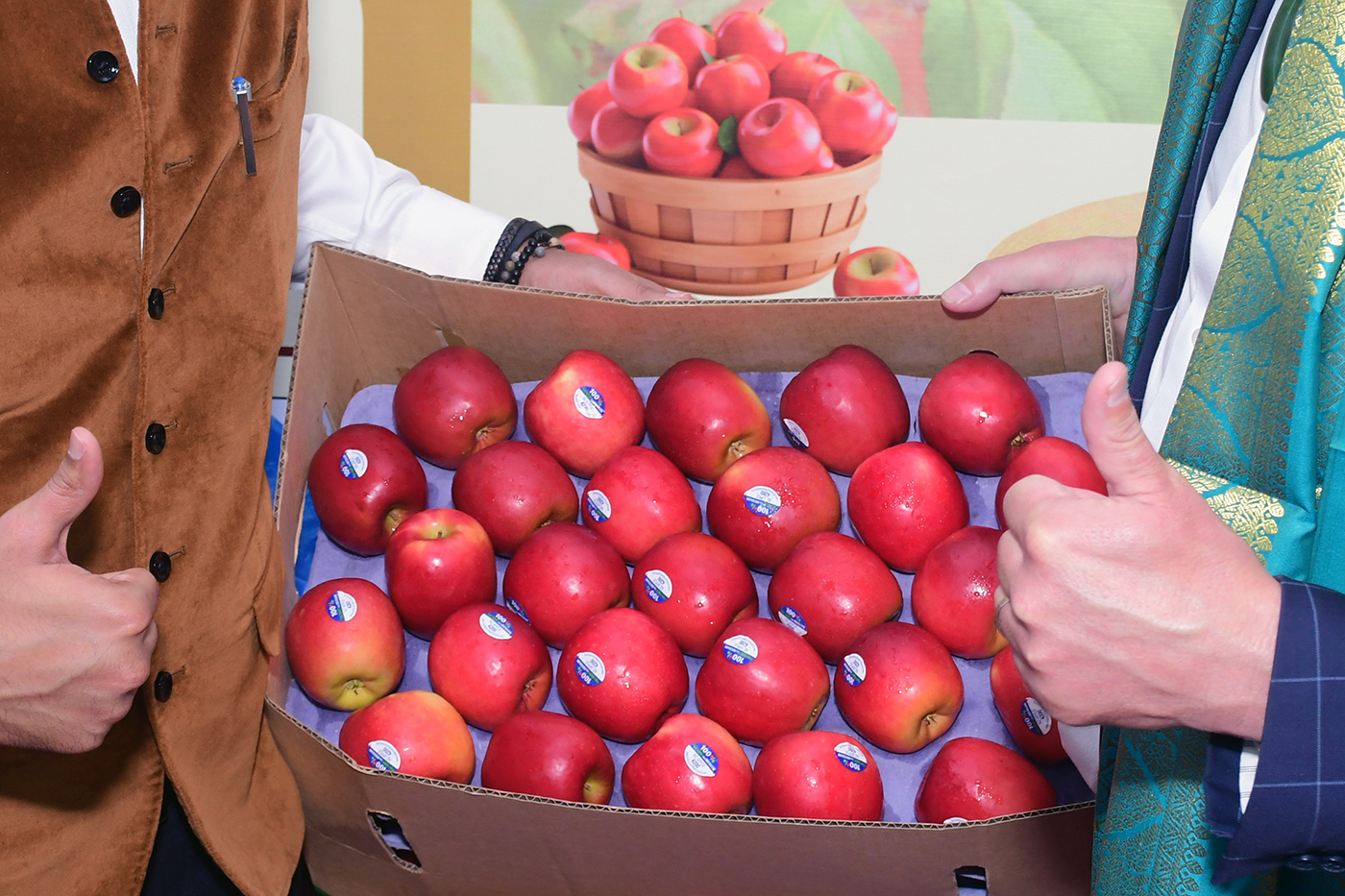 Two men give the thumbs up over a box of red apples