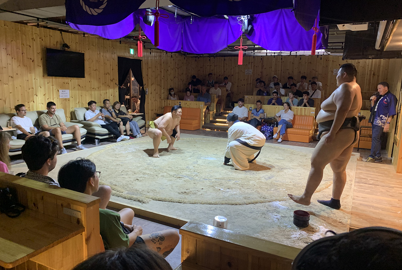 Two men face off for a sumo wrestling match, watched by players from the Sacred Heart College rugby team