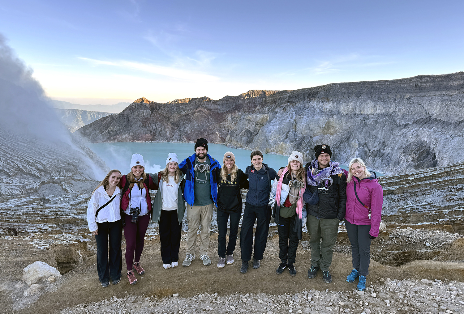 Olivia with a group of friends posing for a photo in front of a volcanic landscape with a lake
