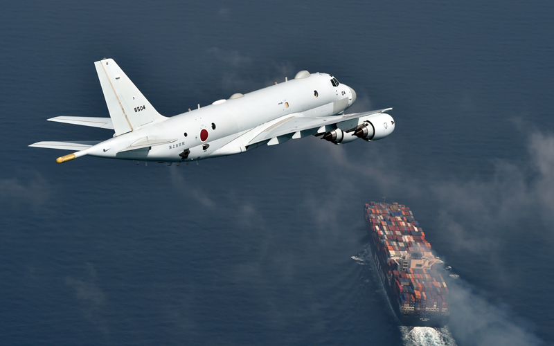 A P-1 surveillance aircraft flying over a container ship