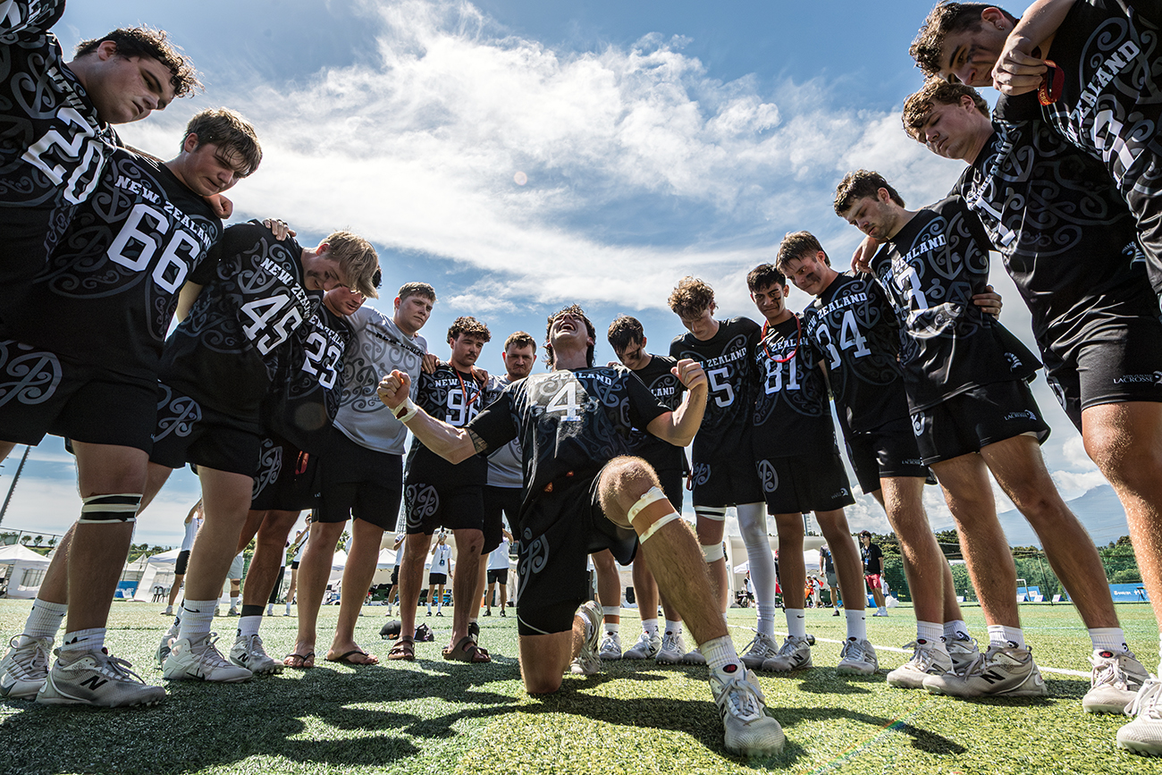 A New Zealand player kneeling on the ground performing a haka surrounded by the rest of the team