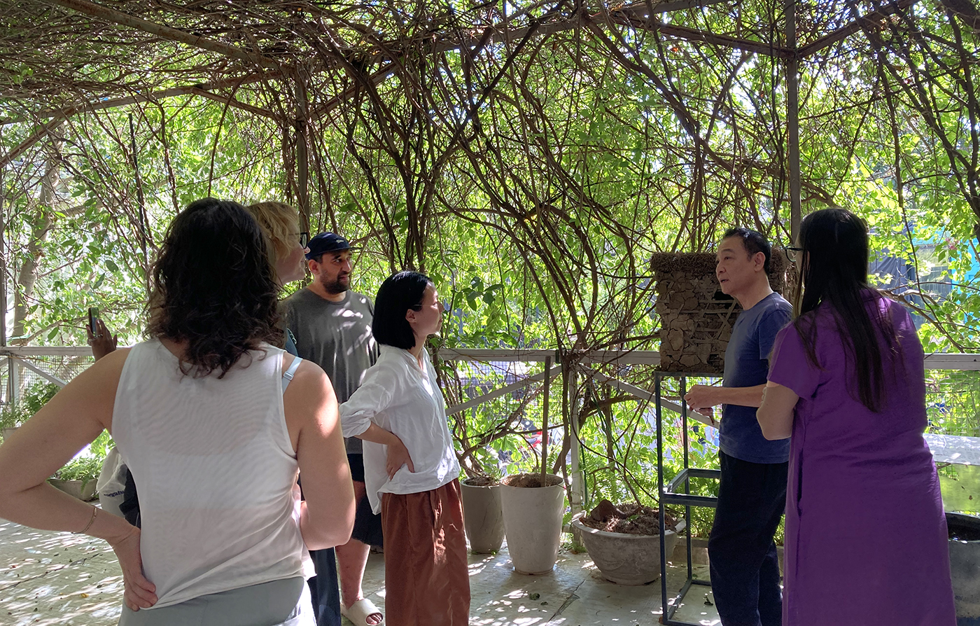 A group of people listening to a man under a pagoda covered in vines