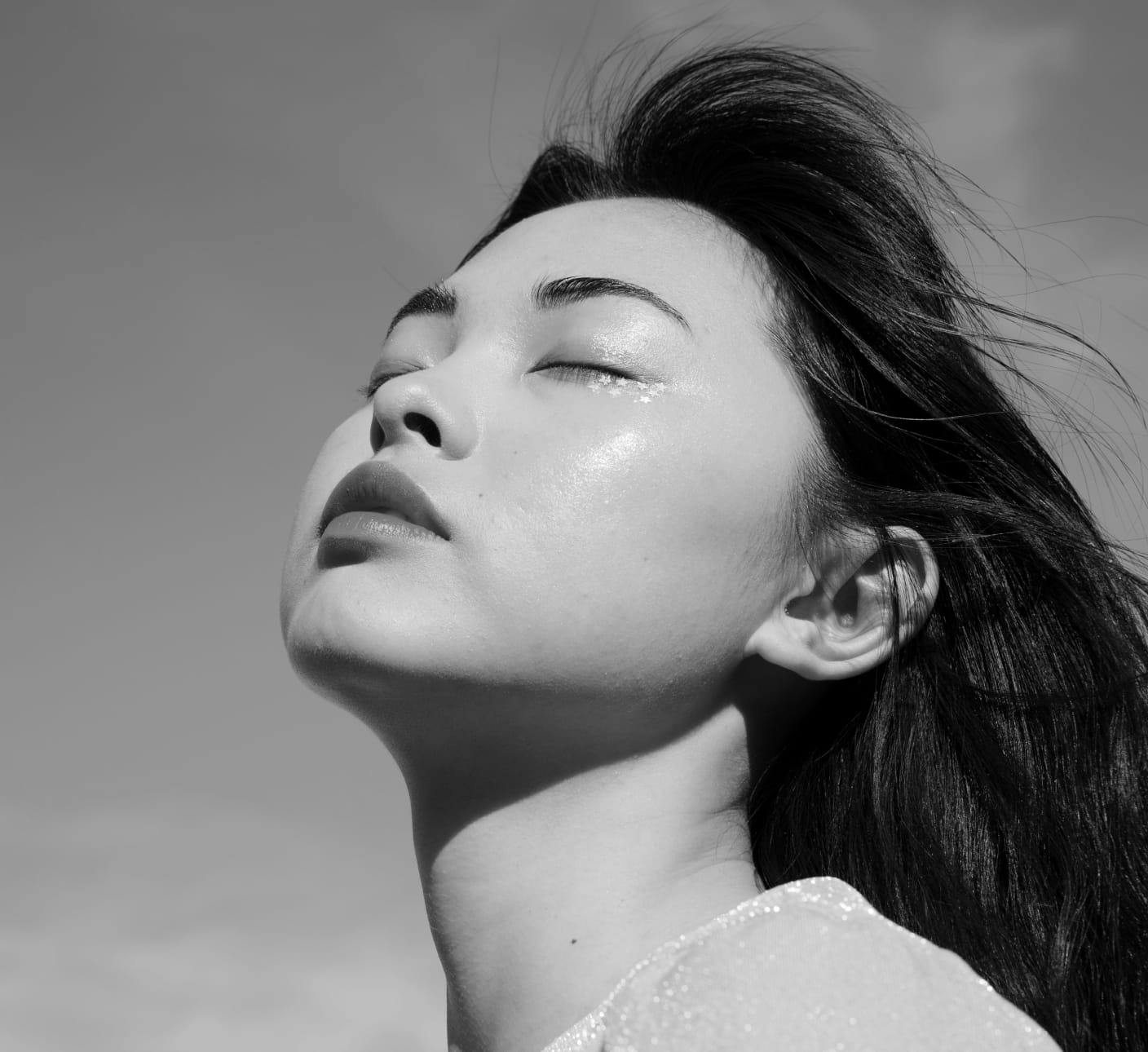Black and white image of a woman facing upwards with her eyes closed