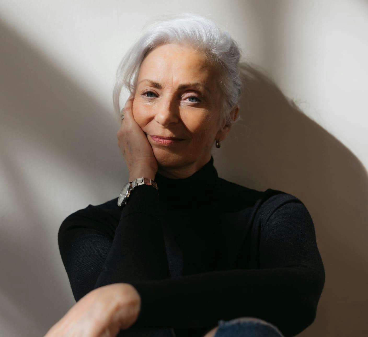 Woman with white hair sitting against a wall