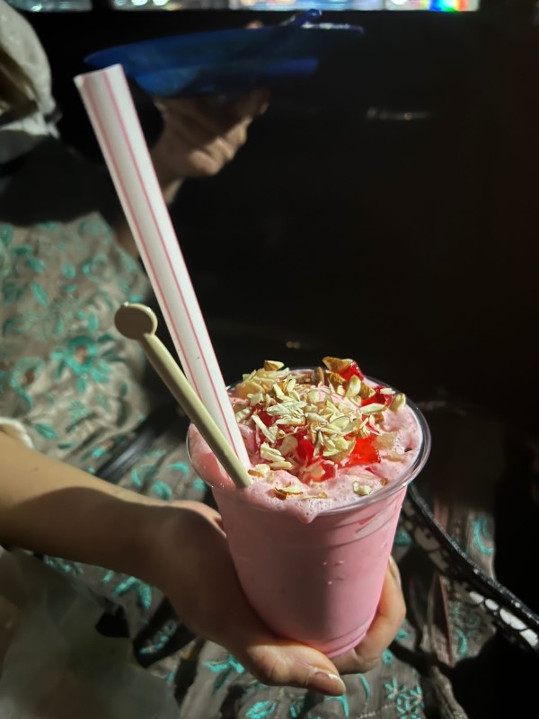 An iced pink drink in a plastic cup, topped with flakes of nuts.
