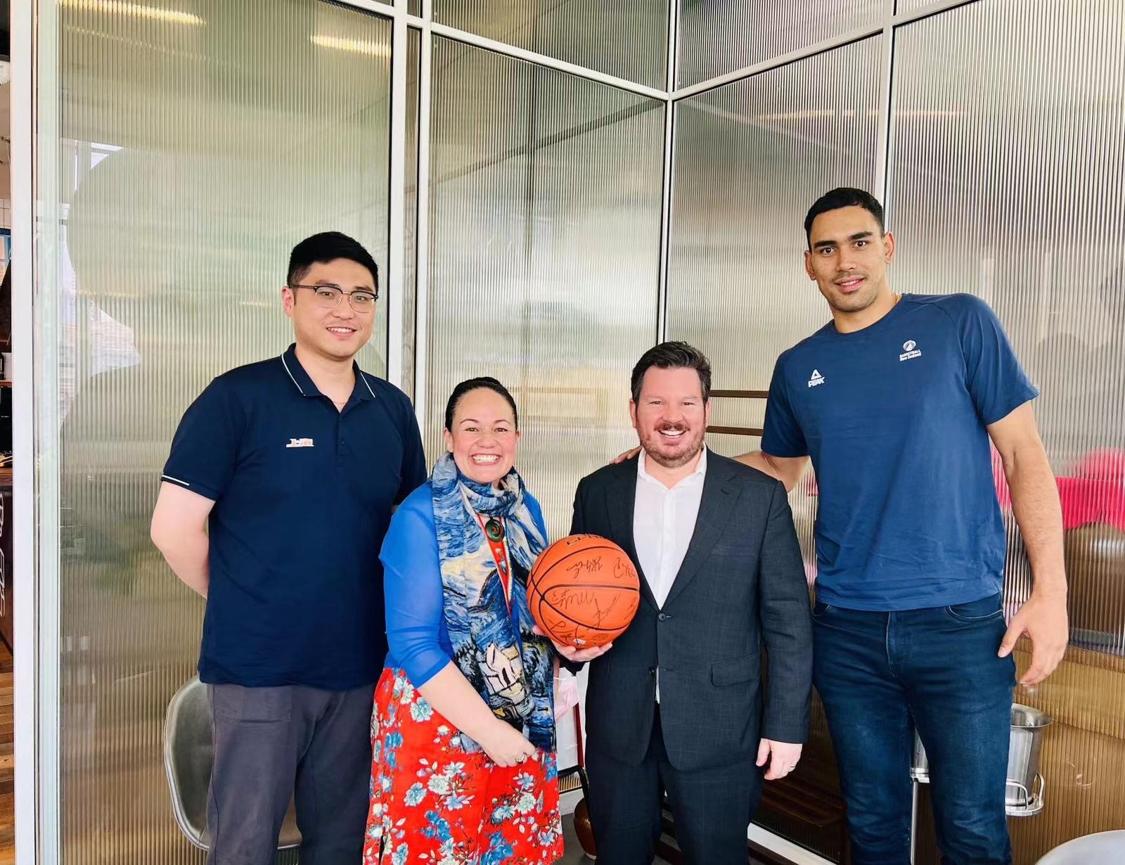 Four people smile at the camera. The central two people hold a basketball