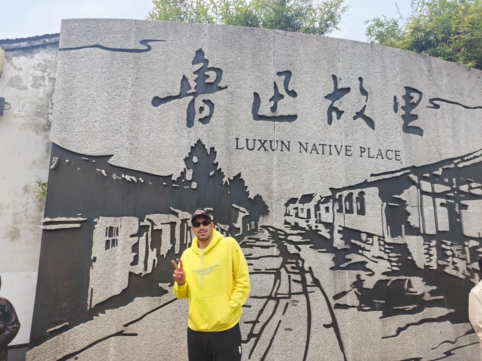 A man in a yellow hoodie stands in front of a painted wall