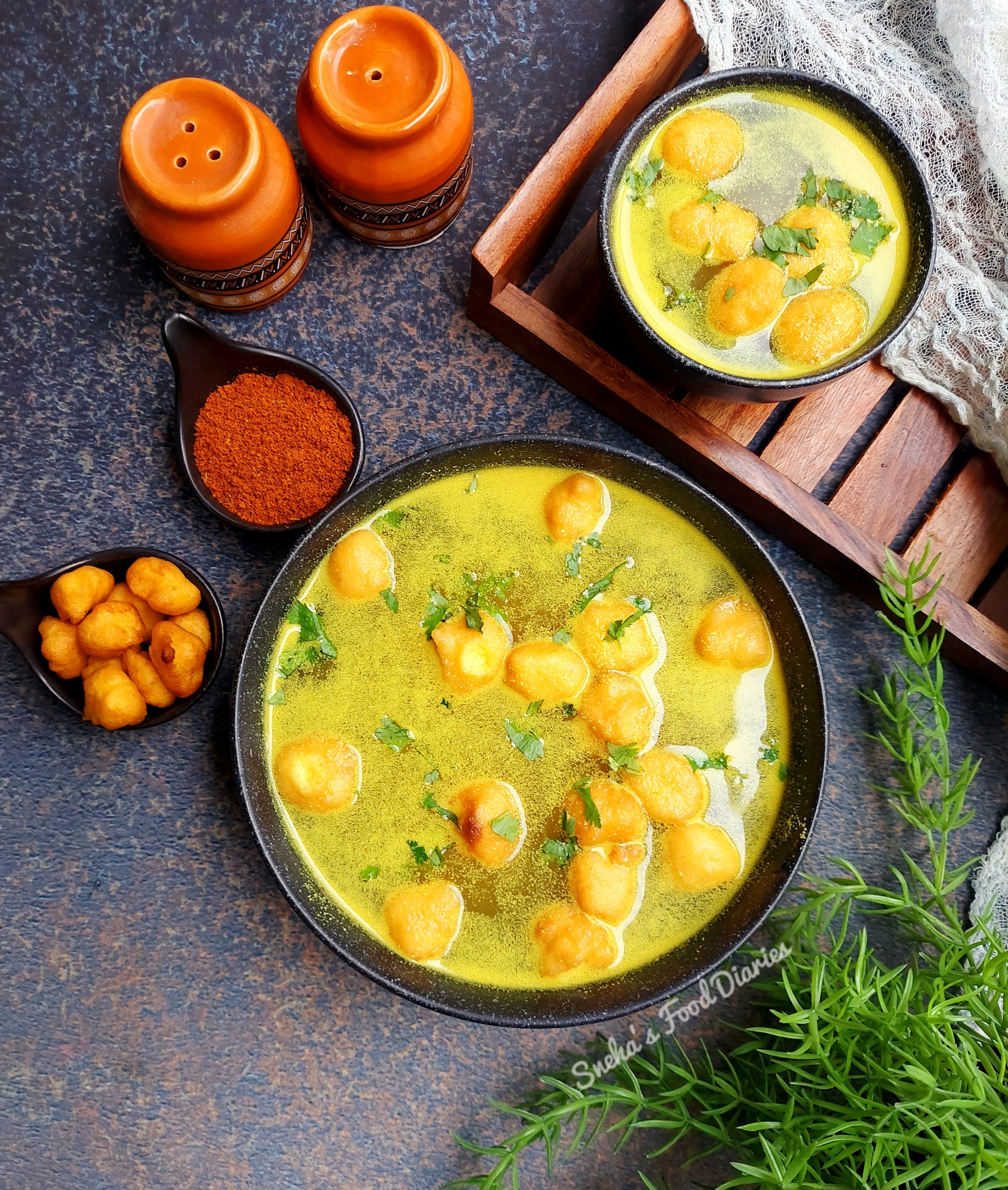 A large bowl of curry-like liquid sits next to spices