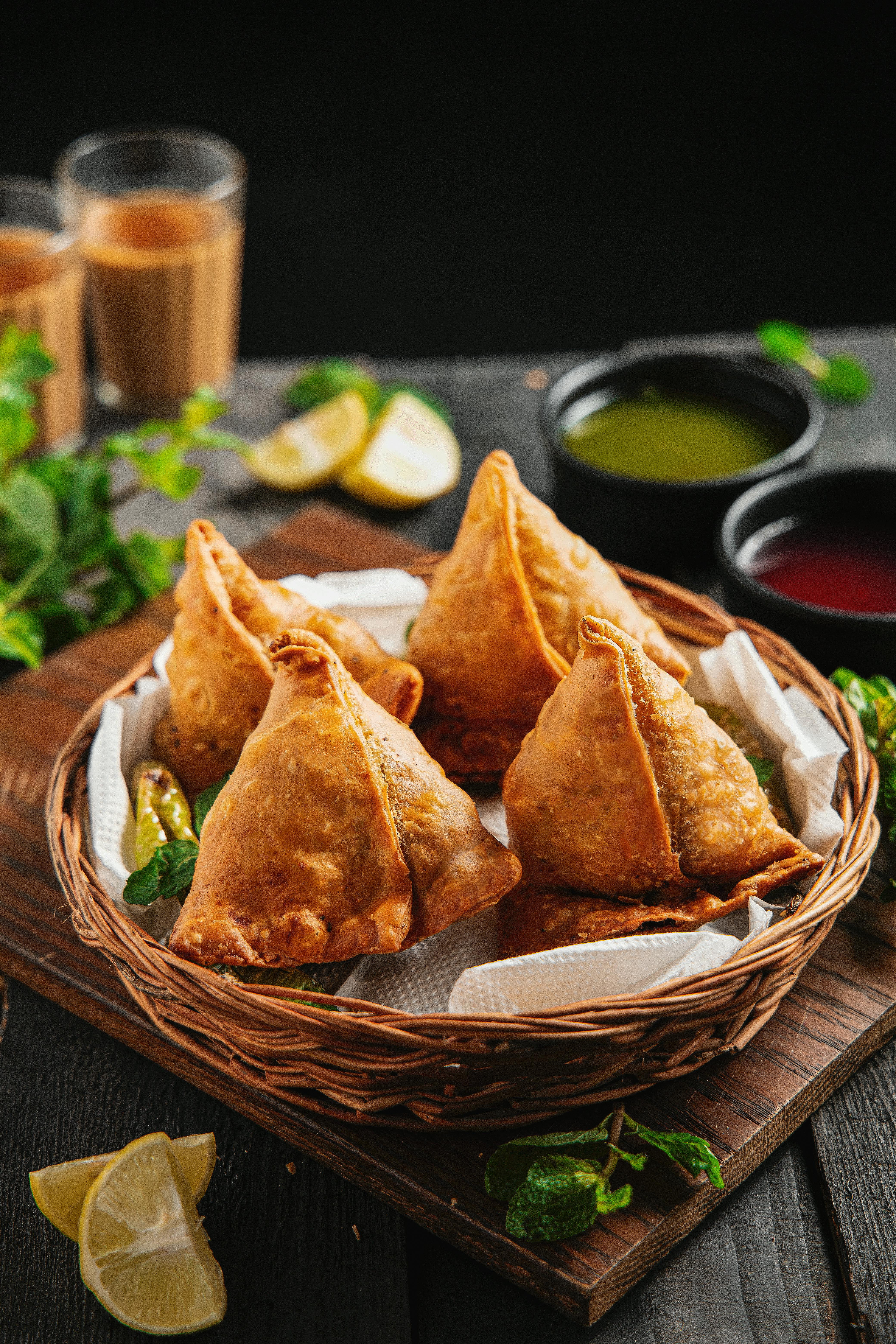 Four crispy samosa sit in a small basket on a table