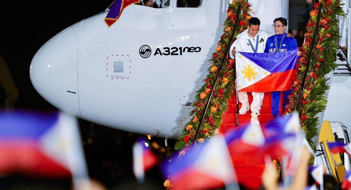 Two men step off a plane onto stairs. Between them they hold a Philippines flag