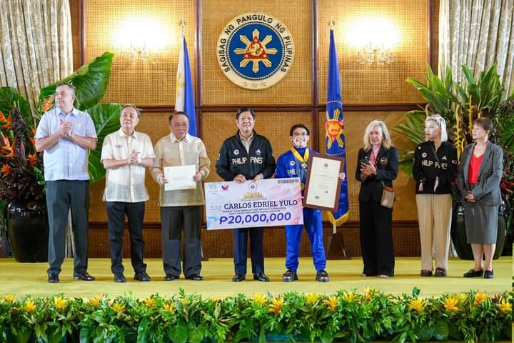 A group stand in line for a photo. The central figure holds a massive check for P20,000,000