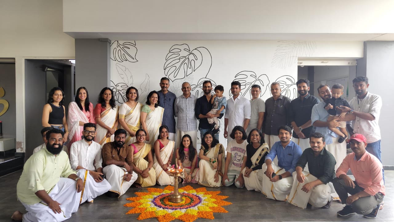 A group of people are lined up, facing the camera. On the ground in front of them is an elaborate orange and white design made of flowers