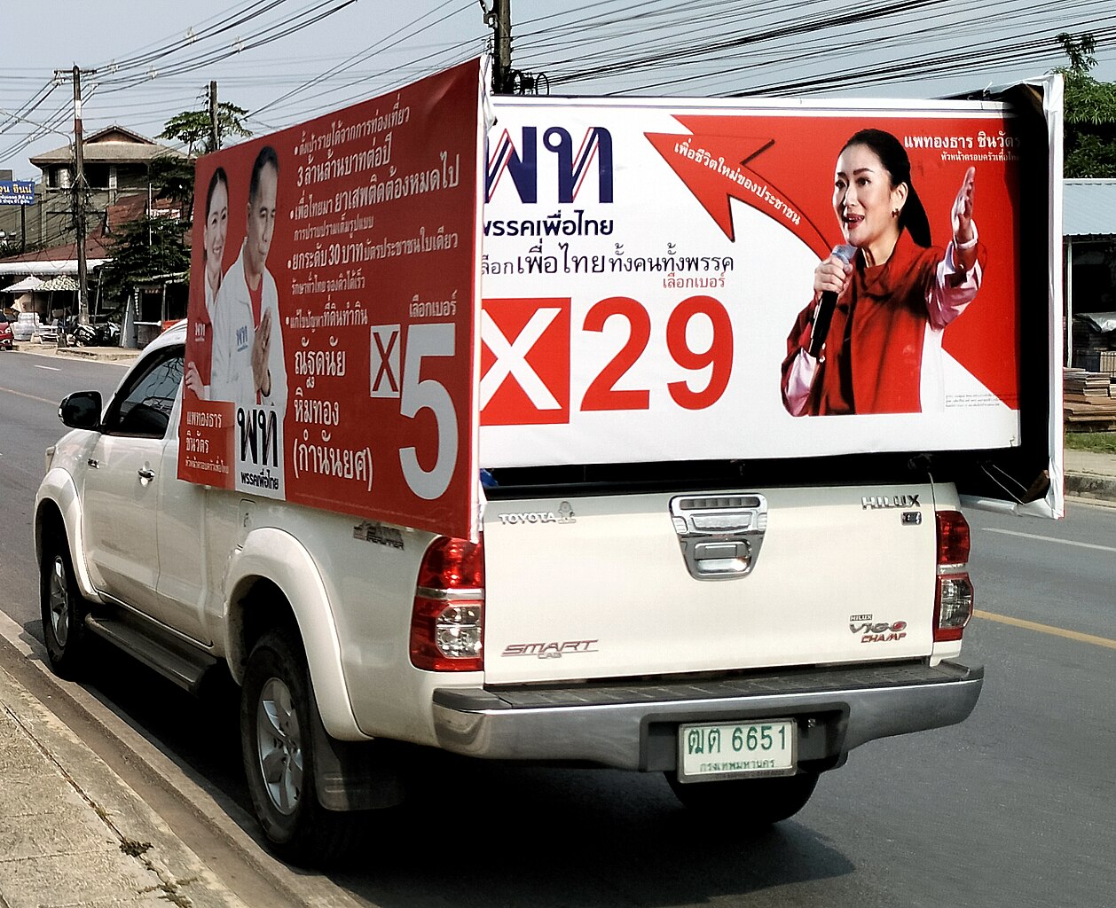 A white ute carries red political signs on the back, featuring a Thai female politician