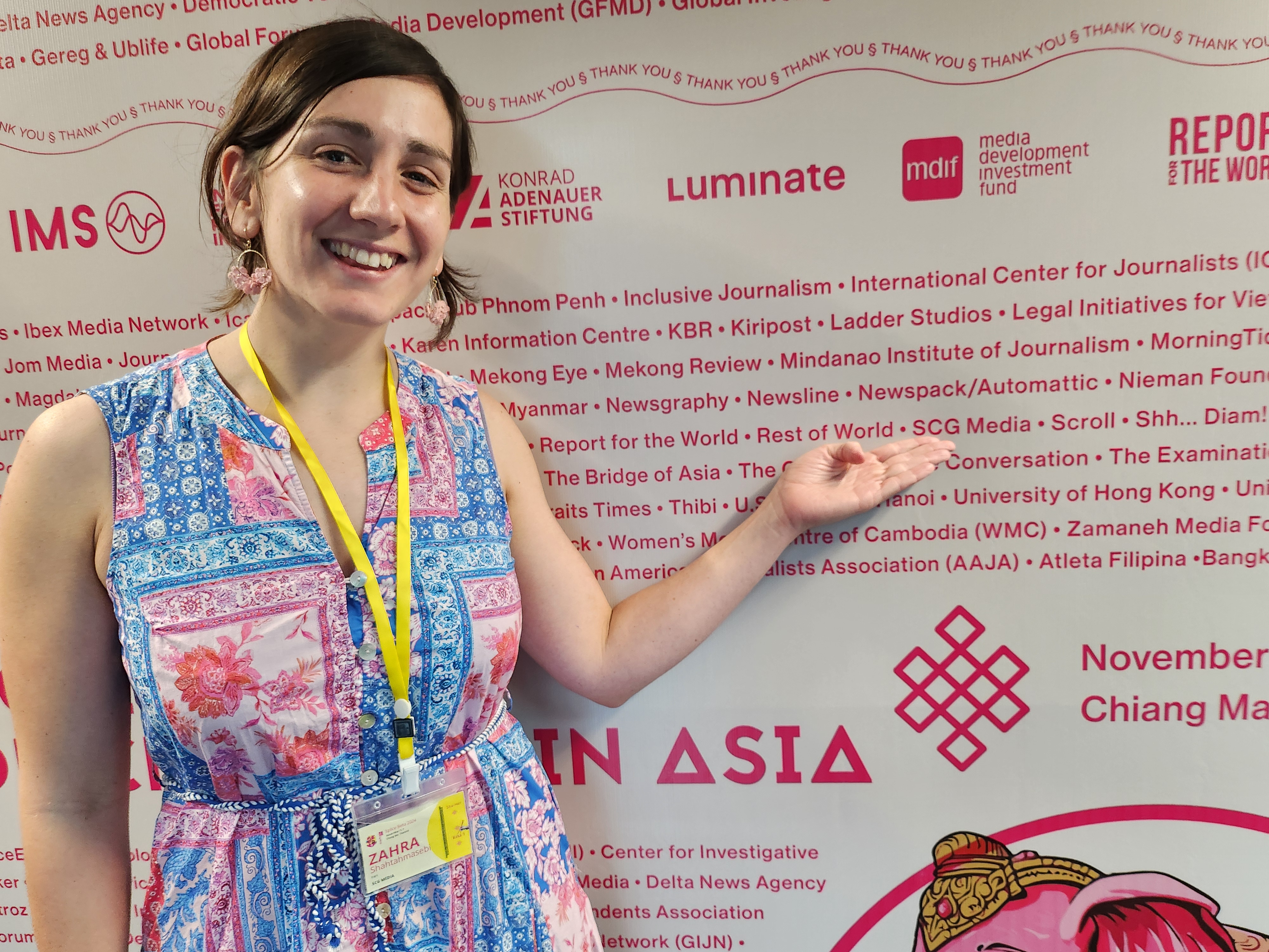 A smiling woman in a colourful dress points to a company name on a list on a wall