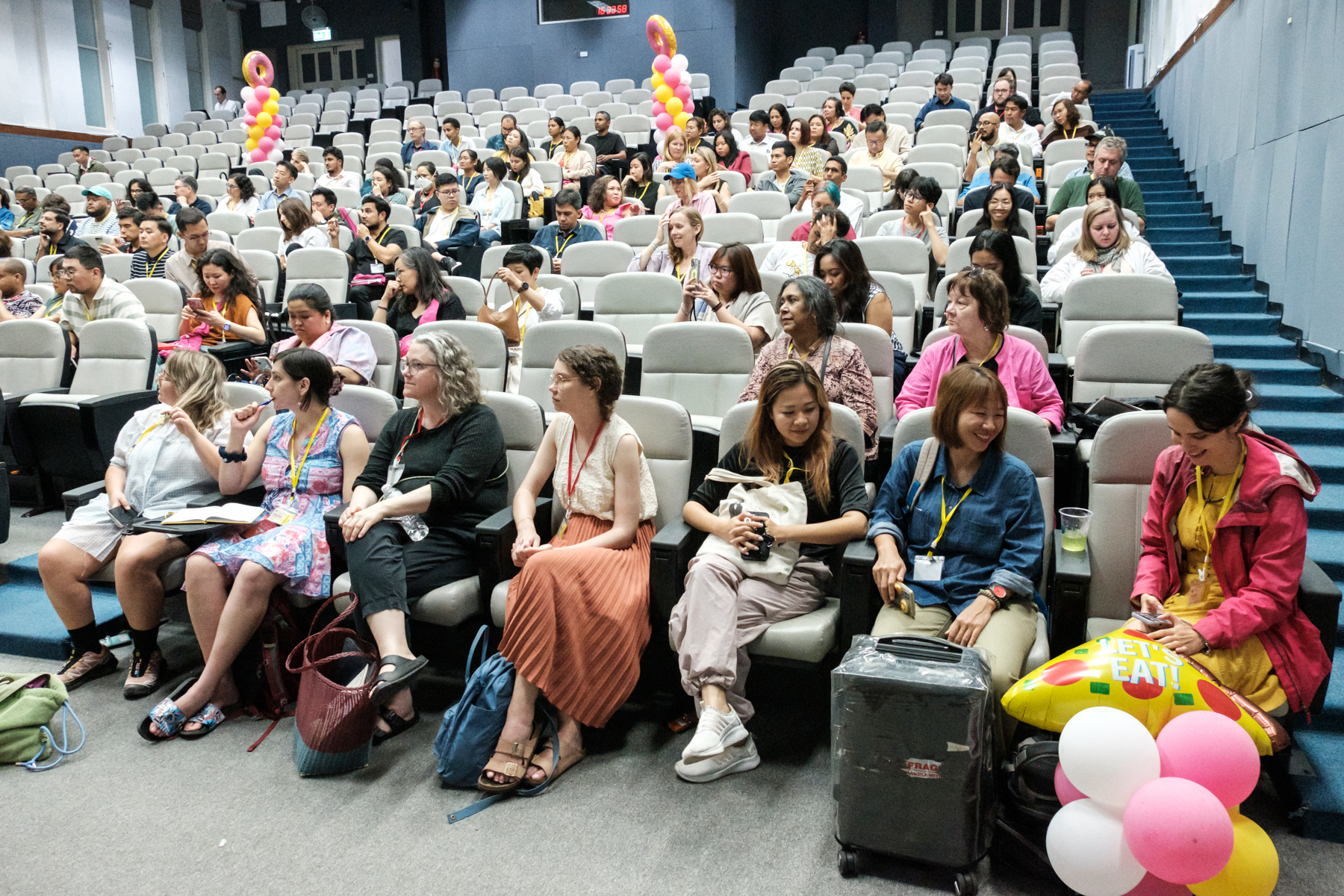 An image of a lecture hall with the seats partially full and attendants looking towards the stage