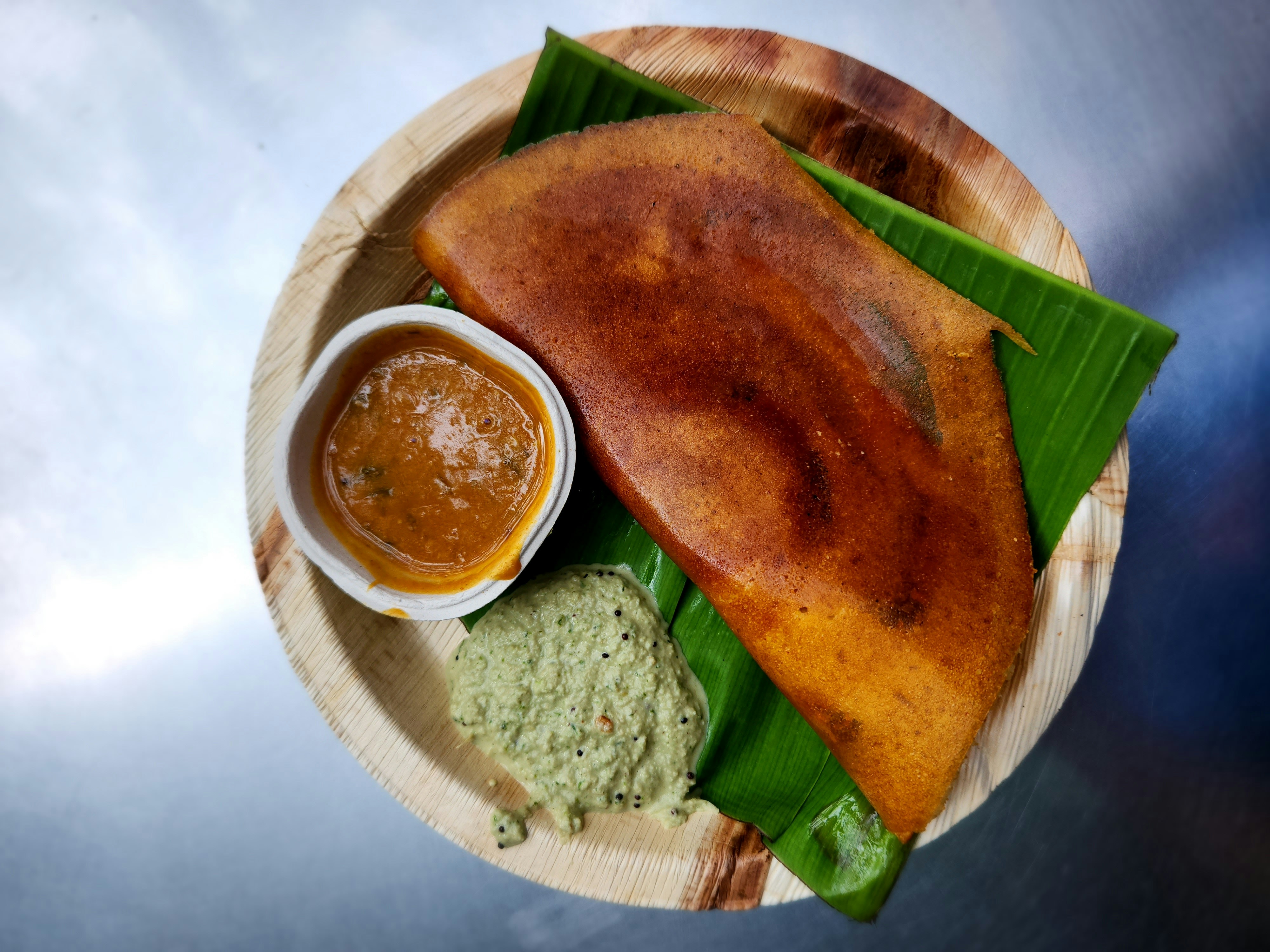 A dosa on a plate with a side of two different pickled dips