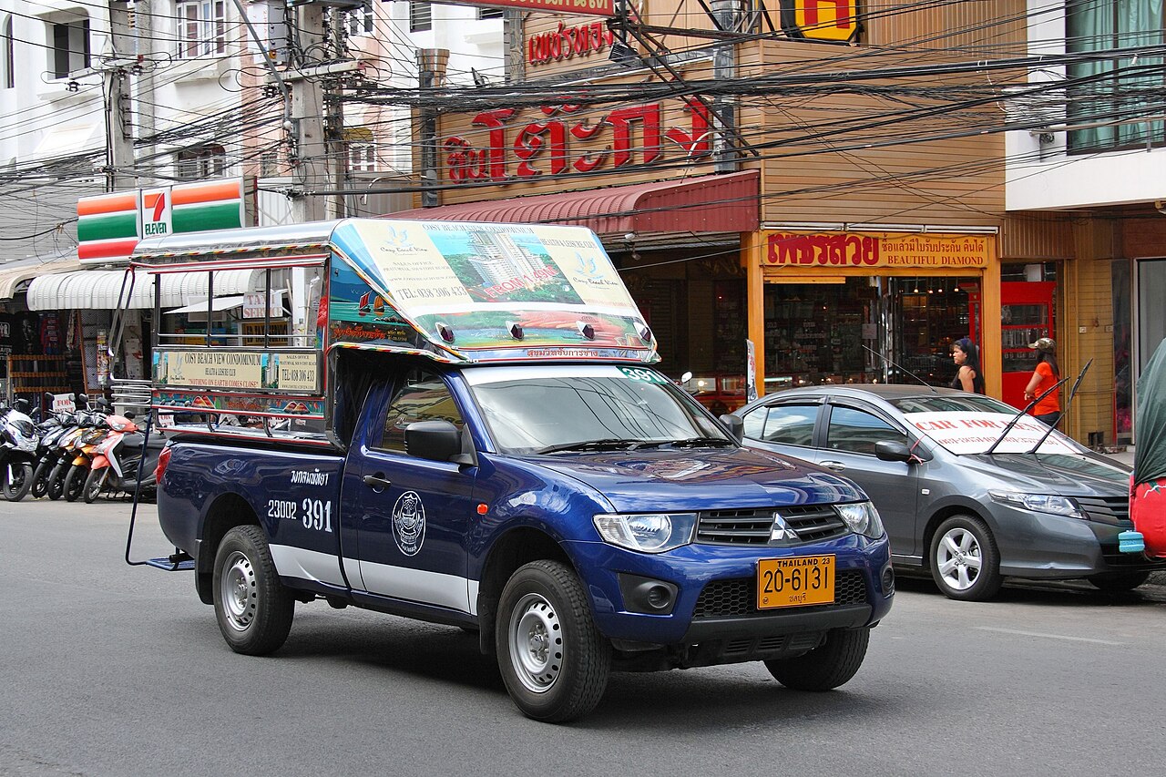 A ute with a covered seating area on the back drives down a street.
