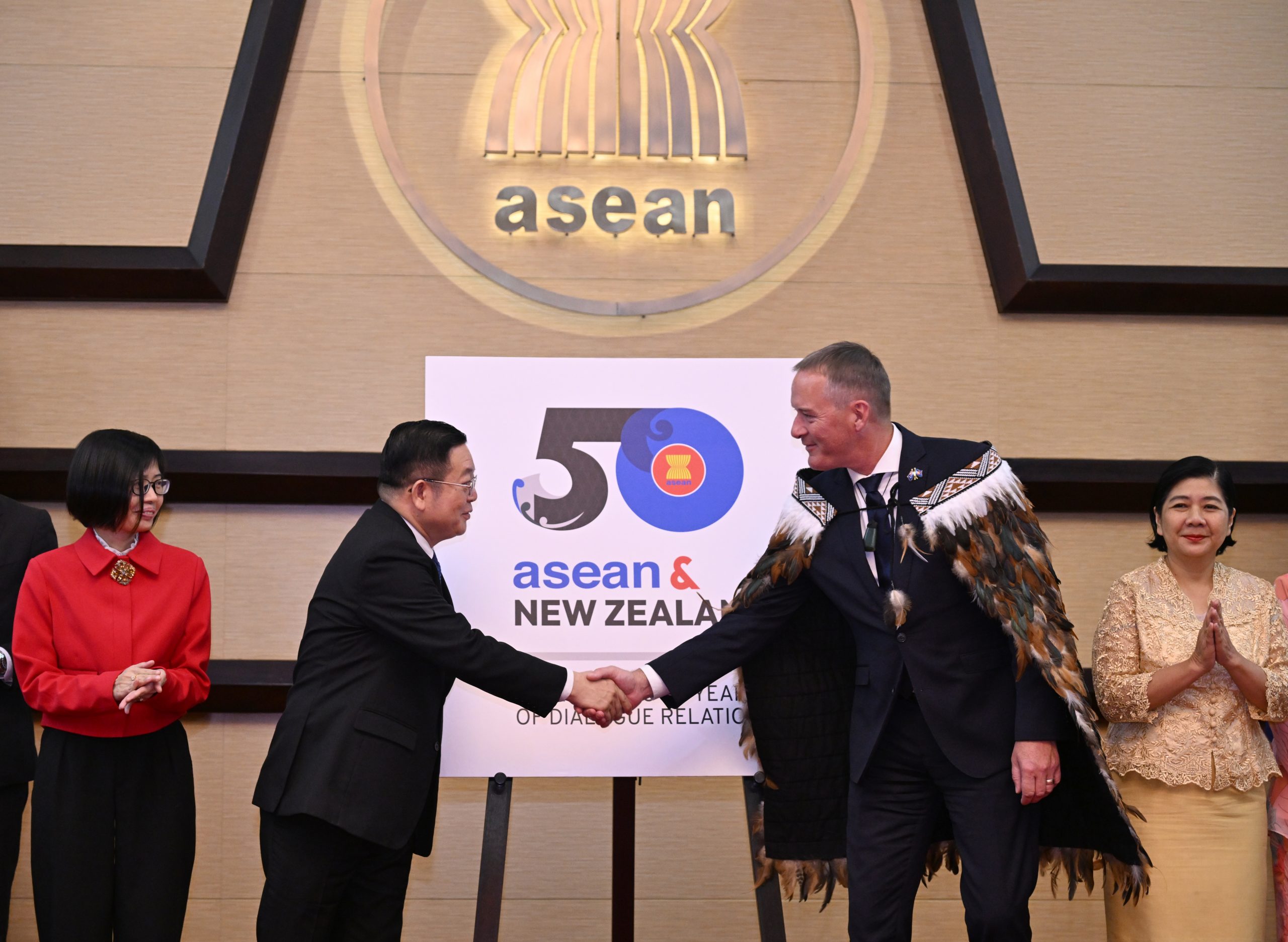 Two men shake hands in front of a sign reading 50 ASEAN and New Zealand