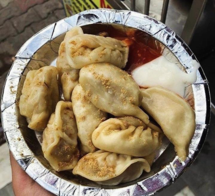 A pile of dumplings of various sizes on a tinfoil plate. Two sauces are on the side.