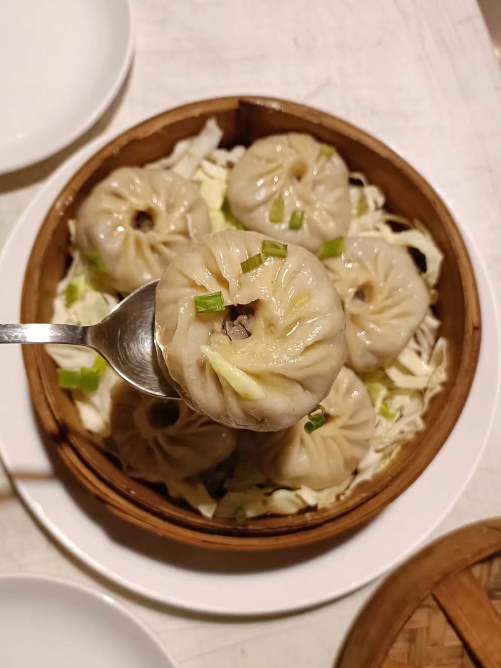 A dumpling with a swirled top sits on a spoon above a bowl full of similar dumplings