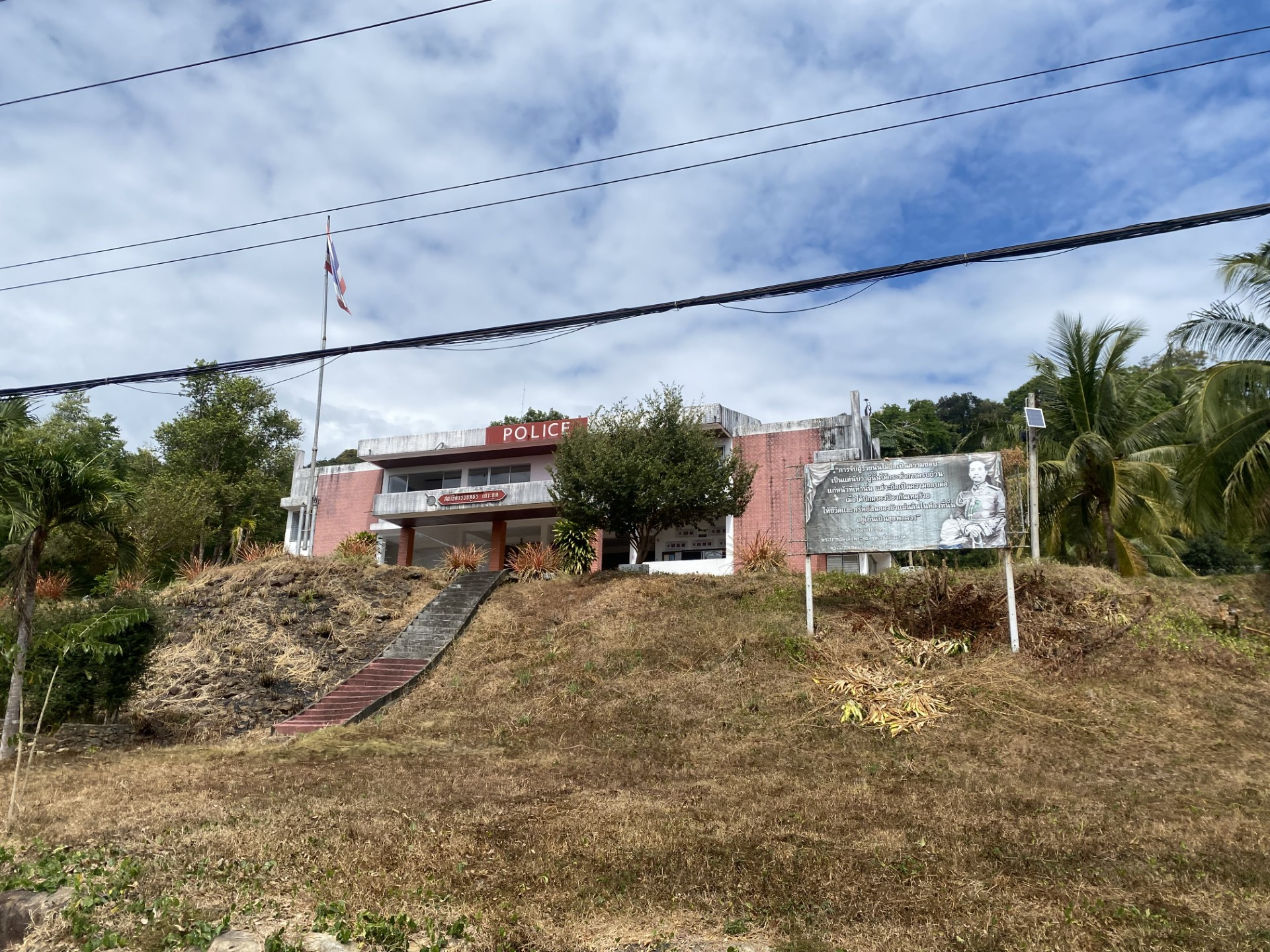 A small police station on a grassy hill, surrounded by palm trees